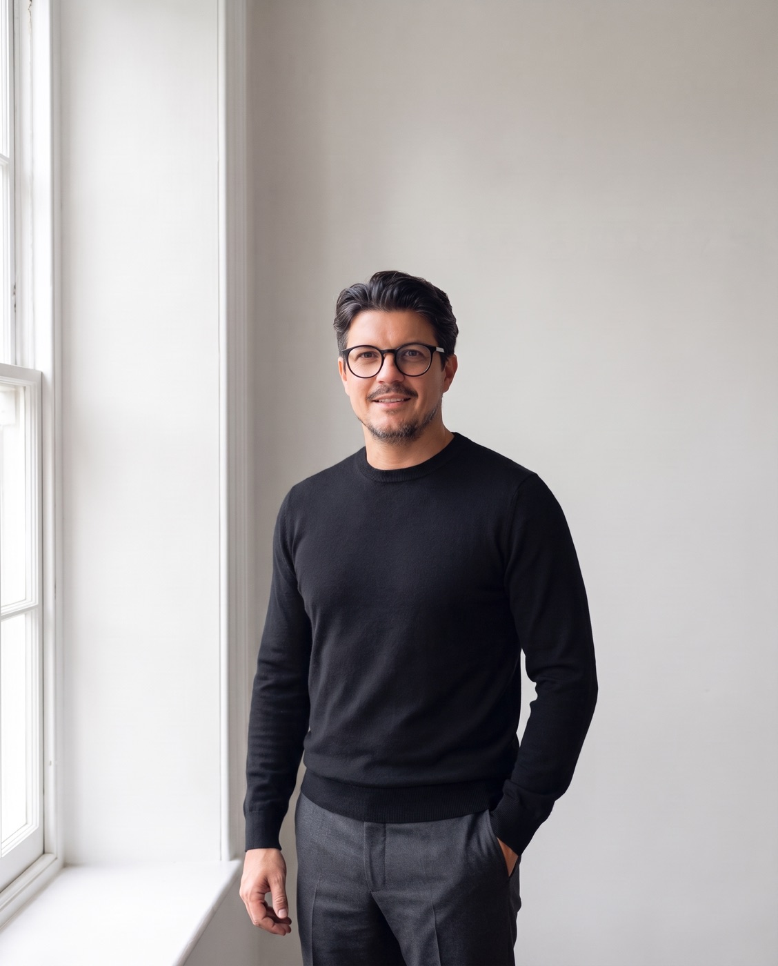 Tom Chard, standing by a window in a black jumper